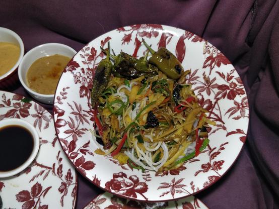 Japchae - koreanisches Nudelgericht mit Gemüse, Pilzen und Tofu. Mit gerösteten grünen Chilis darauf.