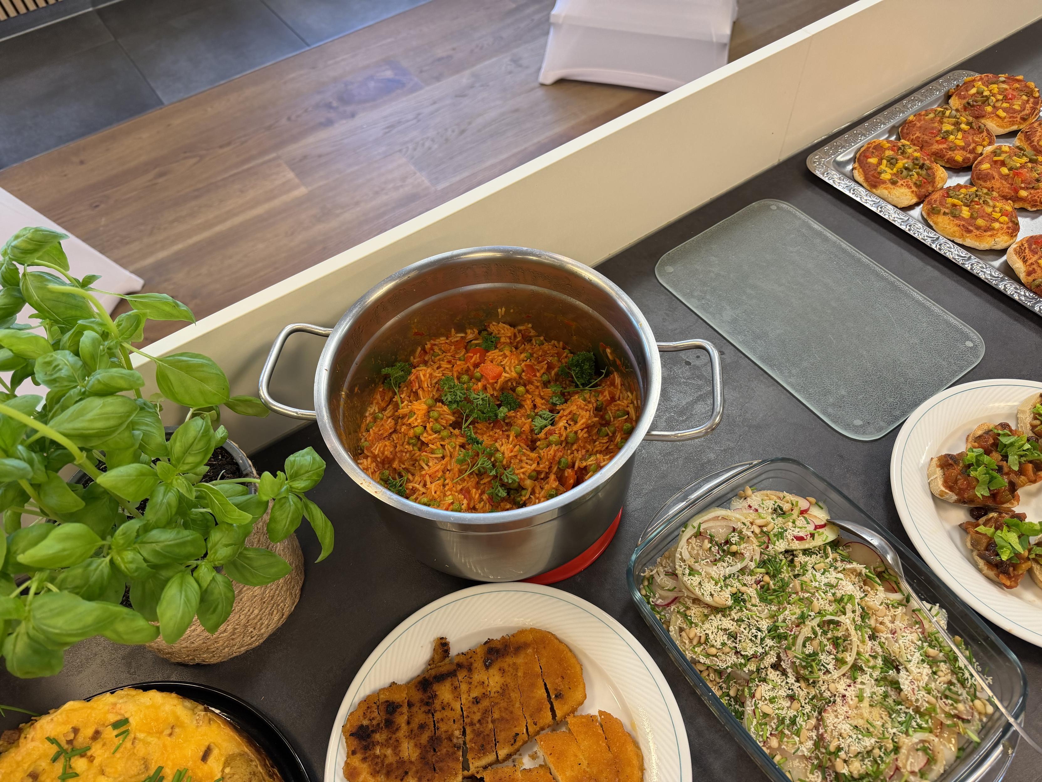 Reich gedecktes Buffet eines veganen Kochkurses mit Mini-Pizzen, Bruschetta, Reisgericht, Aufläufen, frischem Basilikum und weiteren pflanzlichen Speisen.
